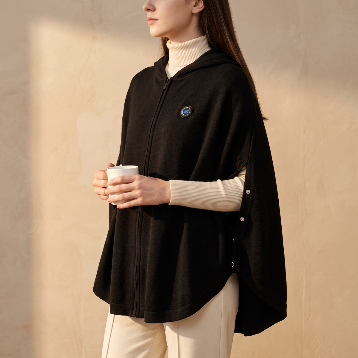 Side view of a woman wearing the black heated knit poncho holding a white mug